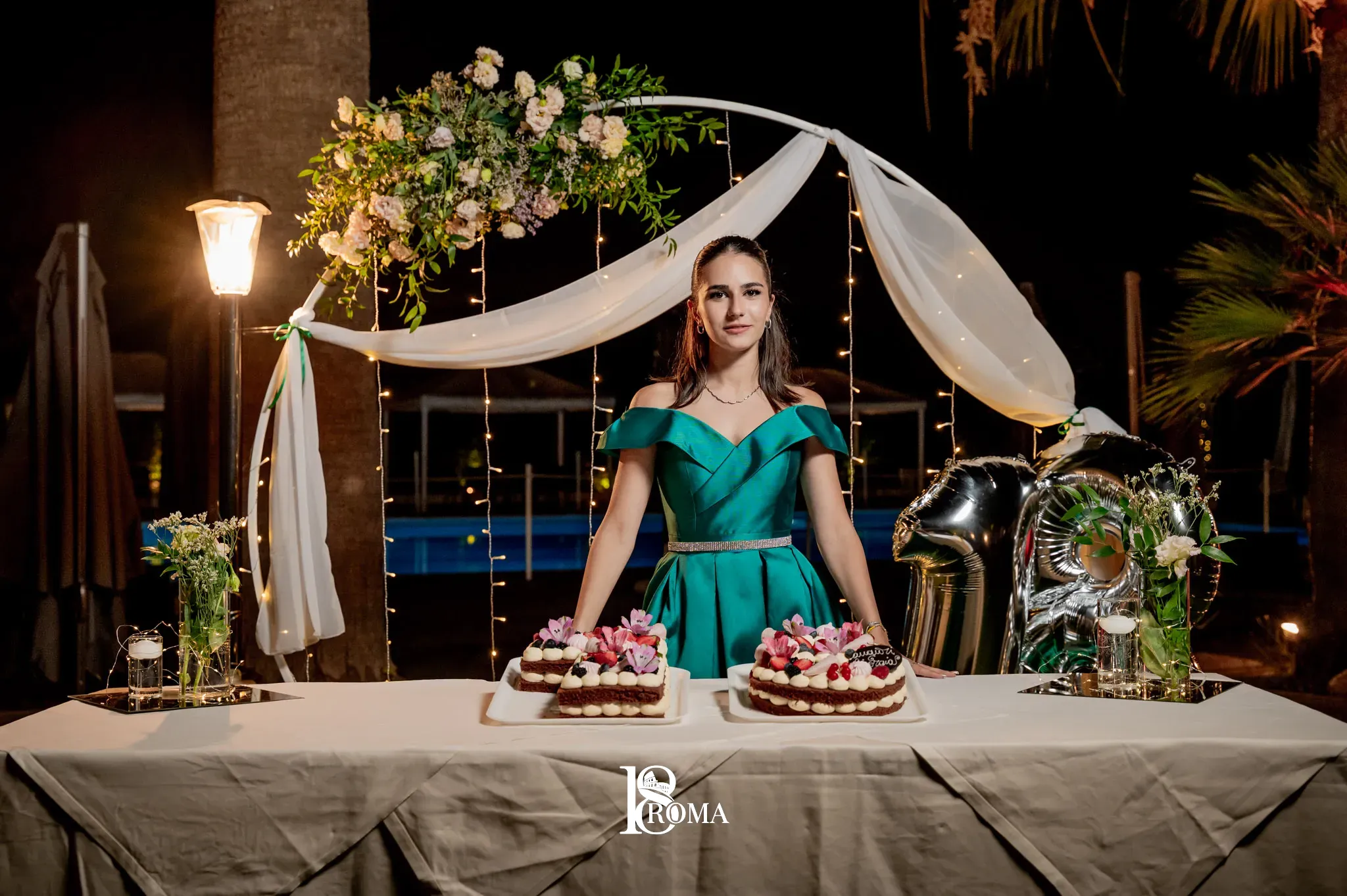 Festeggiata in abito verde al tavolo della torta sotto un arco di fiori