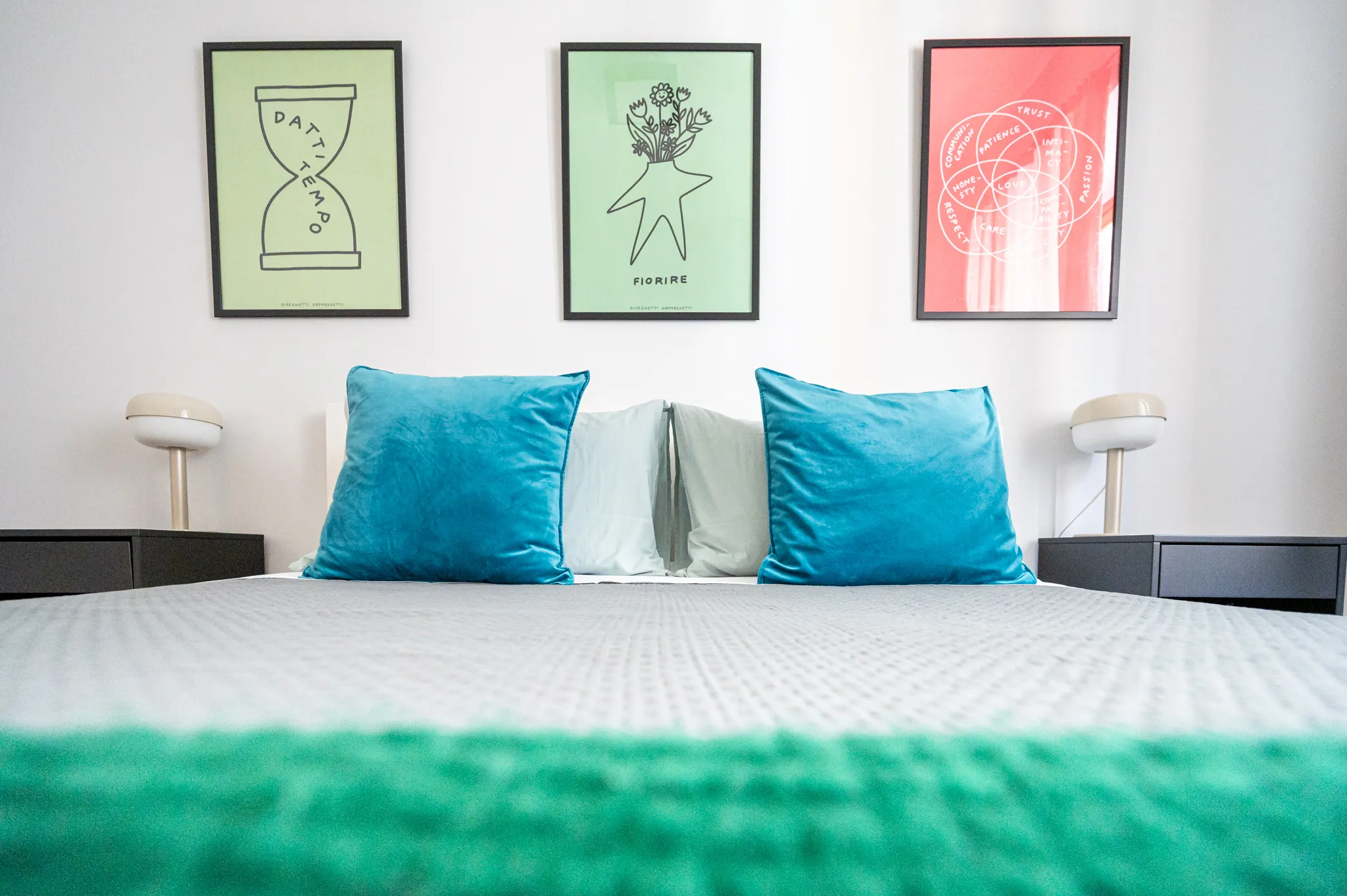 Letto con cuscini turchese sotto tre poster colorati incorniciati