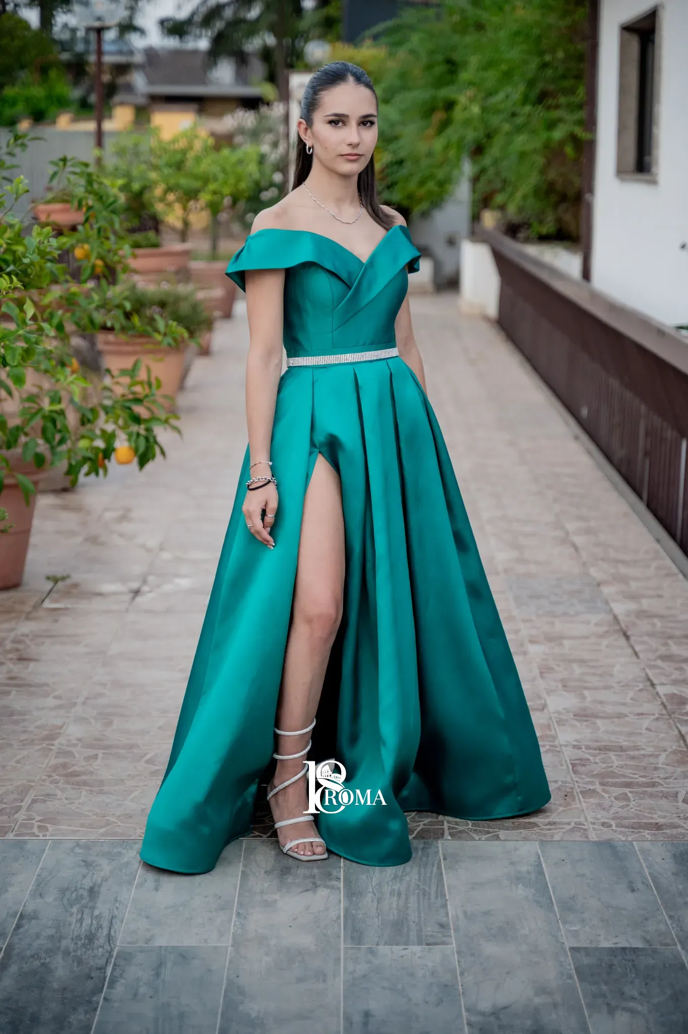 Ragazza in abito lungo verde smeraldo in posa su una terrazza con piante di agrumi