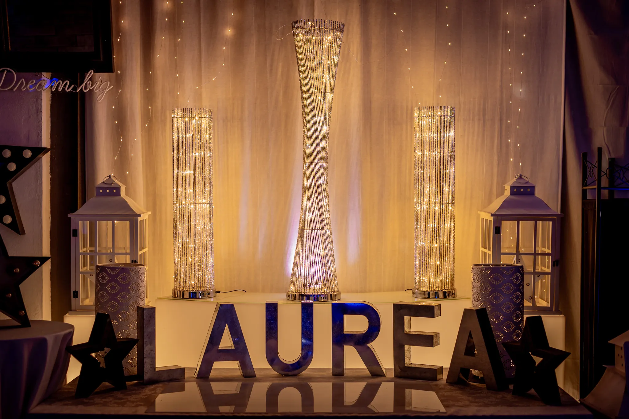 Scritta luminosa LAUREA con lanterne e colonne di luce nell’allestimento di una festa